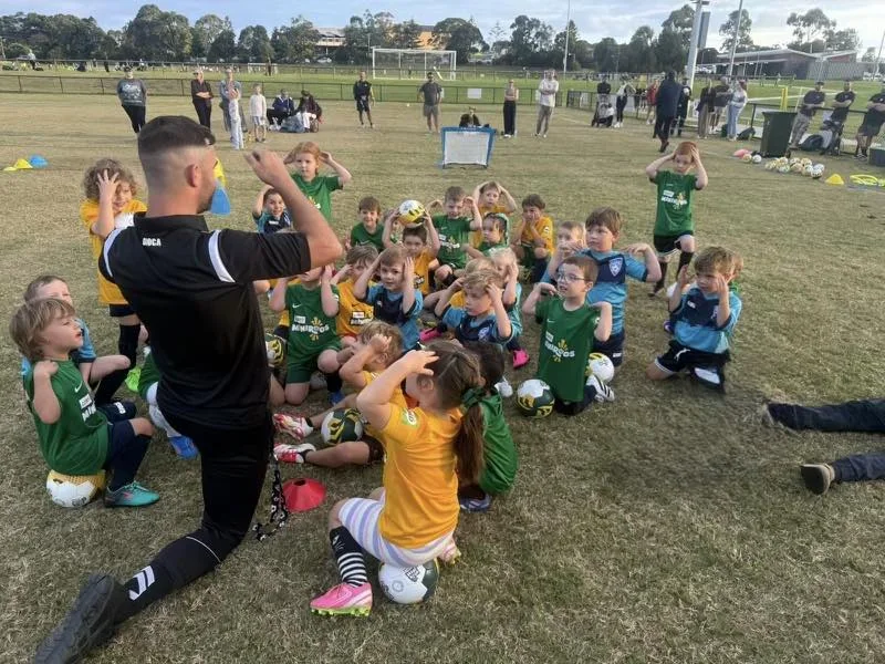 Junior football players listening to a coach during a Shellharbour City Football Club training session
